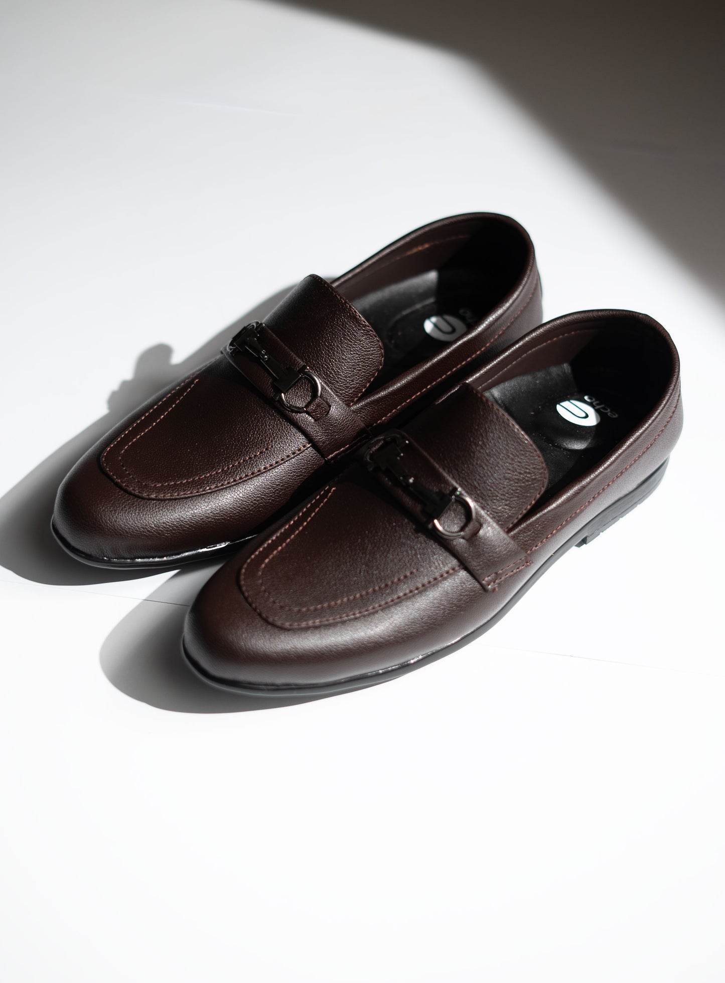 Pair of brown leather loafers on a white surface with a soft shadow.