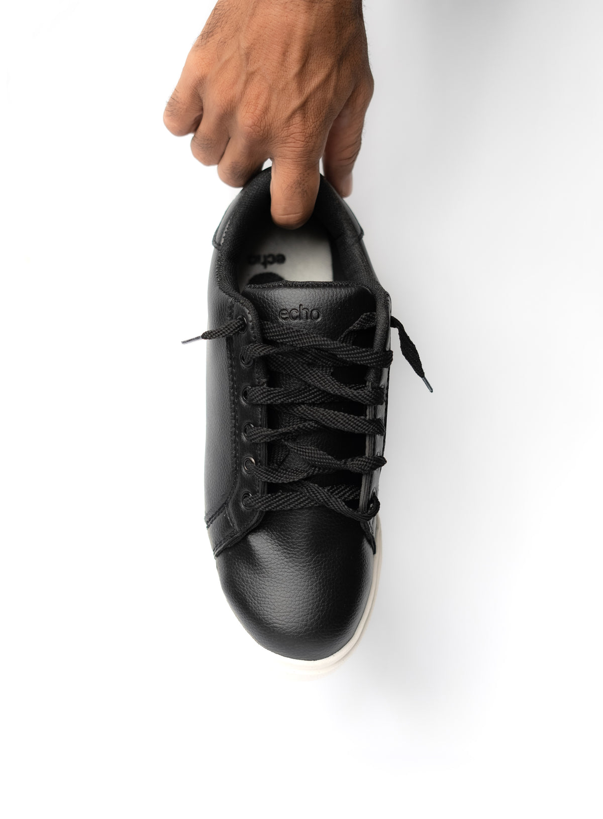 Black sneaker being held by a hand on a white background