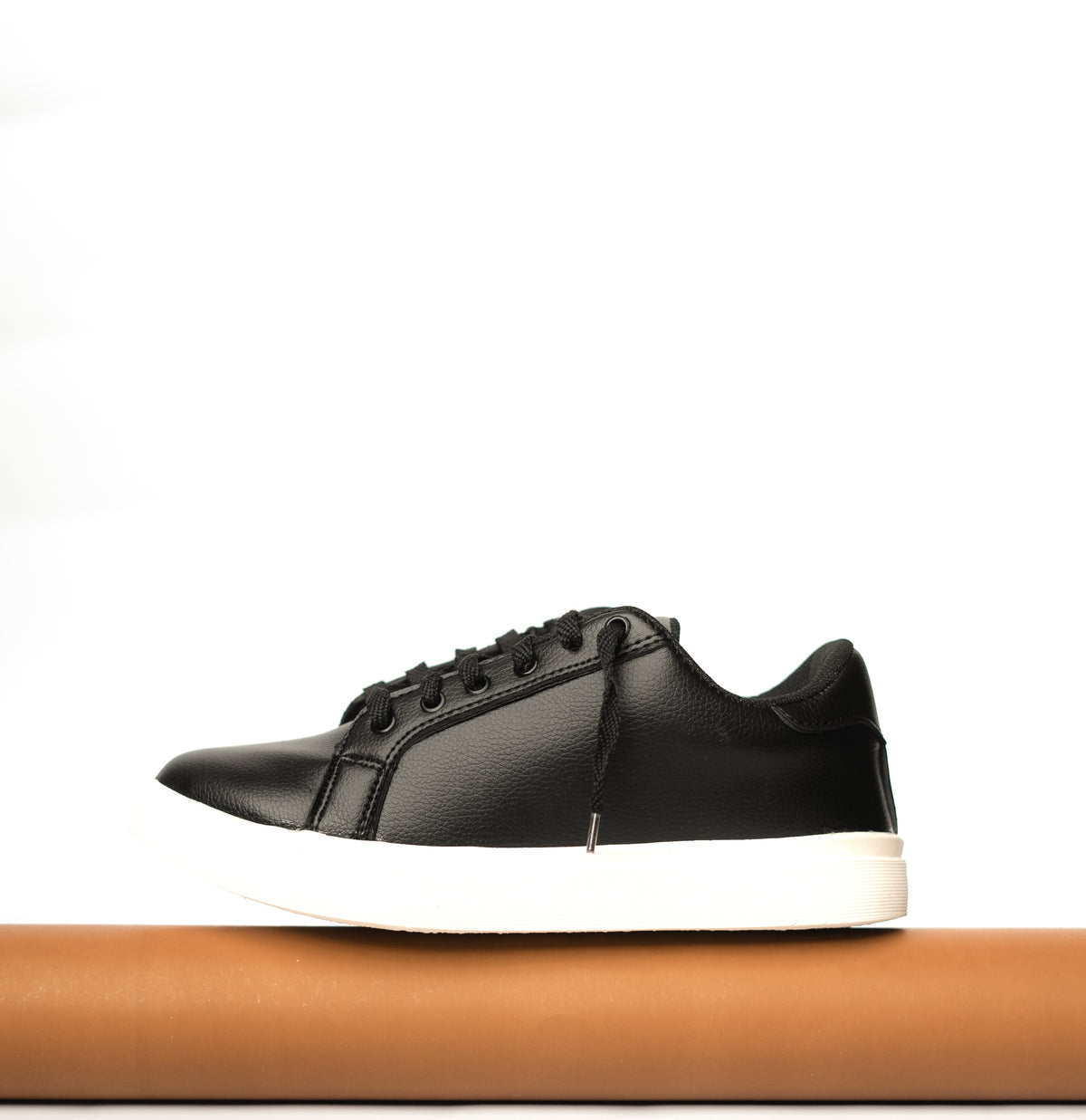 Black leather sneaker with white sole on a wooden block against a white background