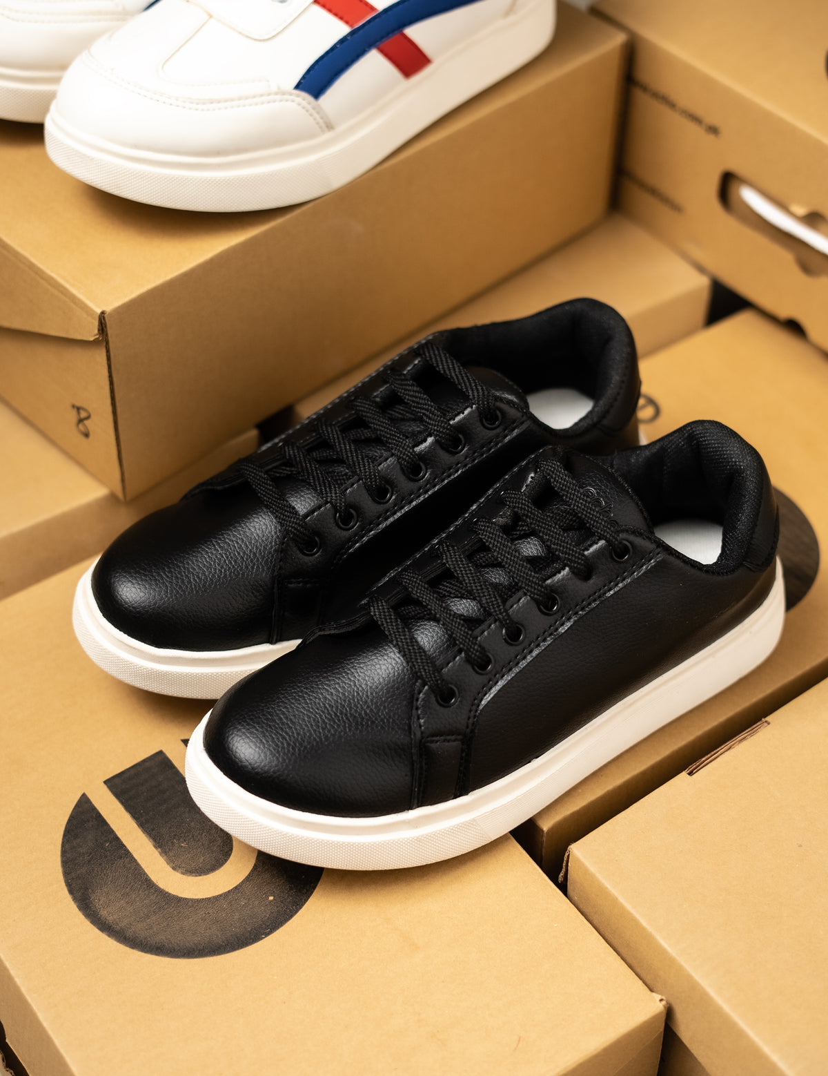 Black sneakers on a cardboard box with a white sneaker in the background