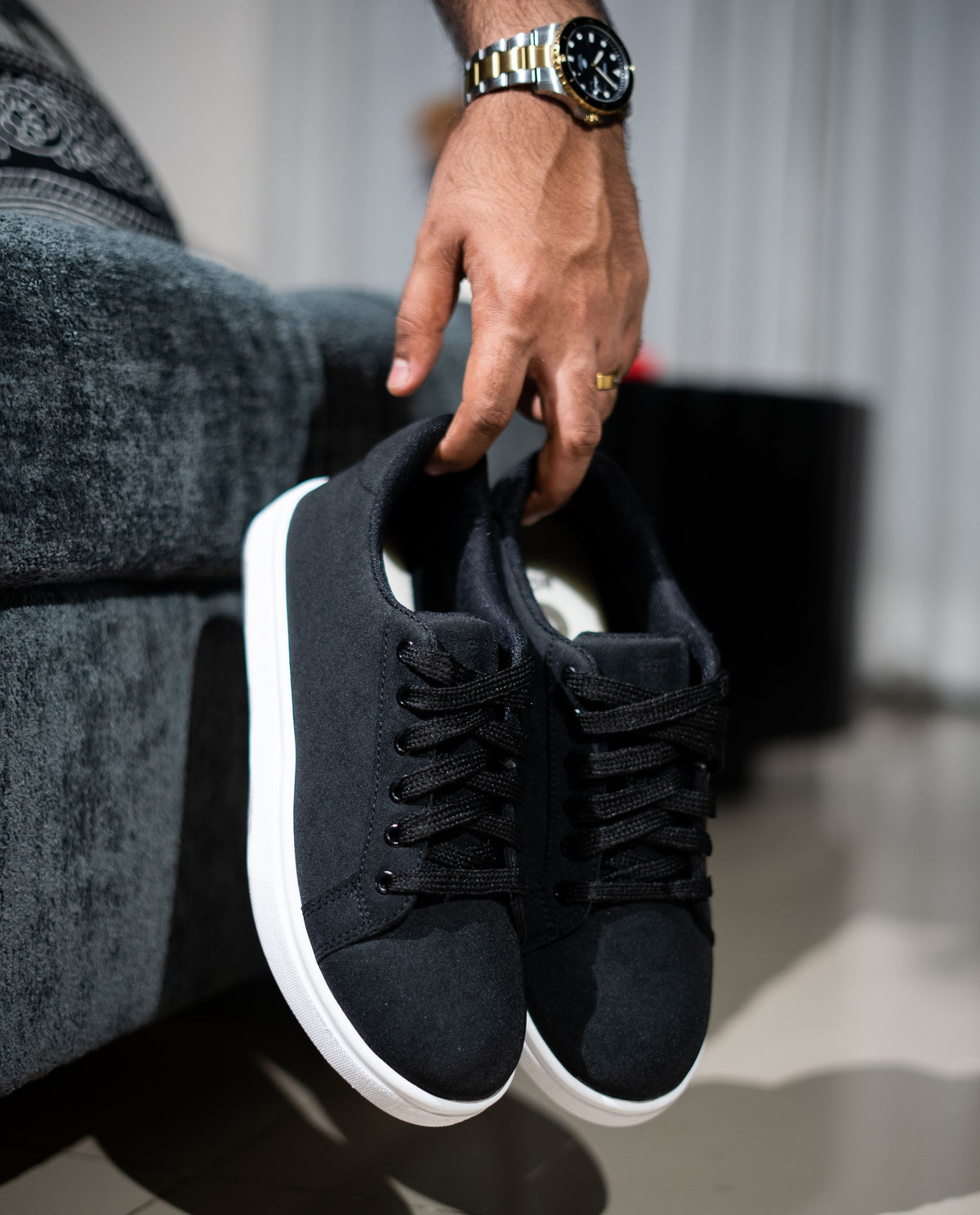 Person holding a black sneaker with white sole on a blurred indoor background