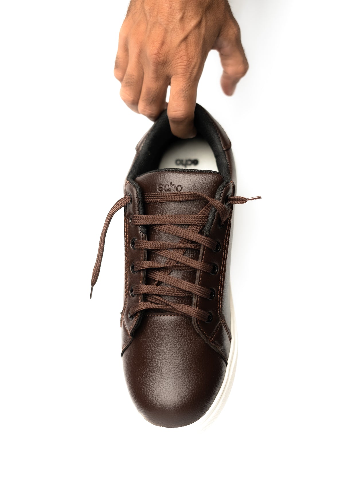 Brown sneaker with white sole held by a hand on a white background