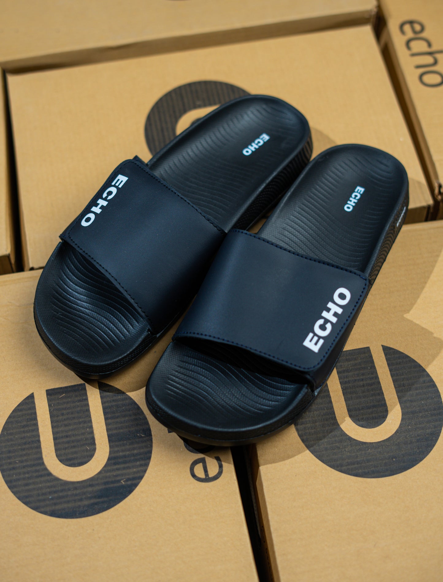 Pair of navy blue slides with 'Echo' branding on a cardboard box background