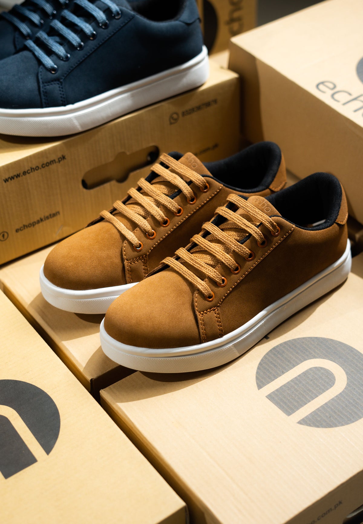 Brown sneakers on Echo brand boxes with a blue sneaker in the background.