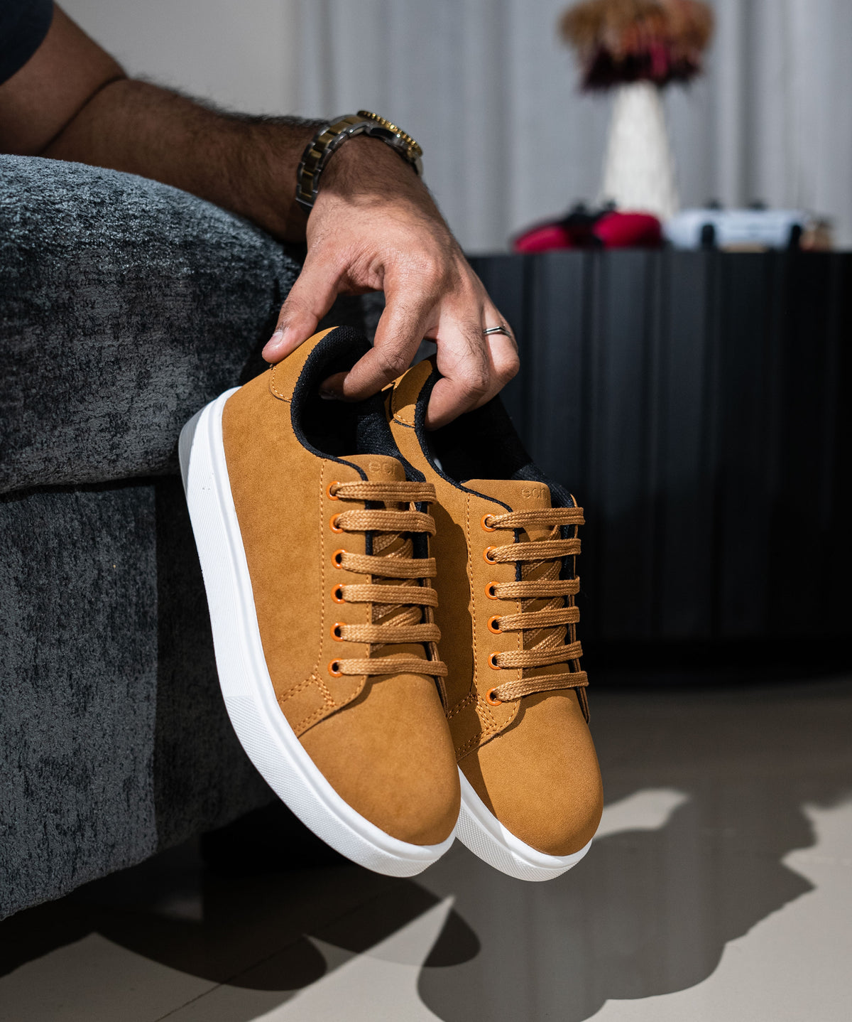 Brown suede sneaker held by a person with a blurred indoor background
