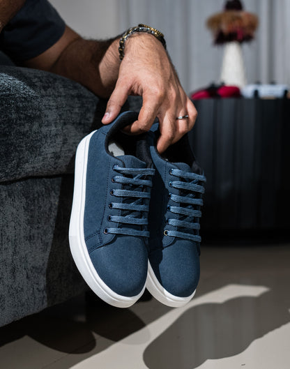Person holding a pair of blue sneakers with white soles.