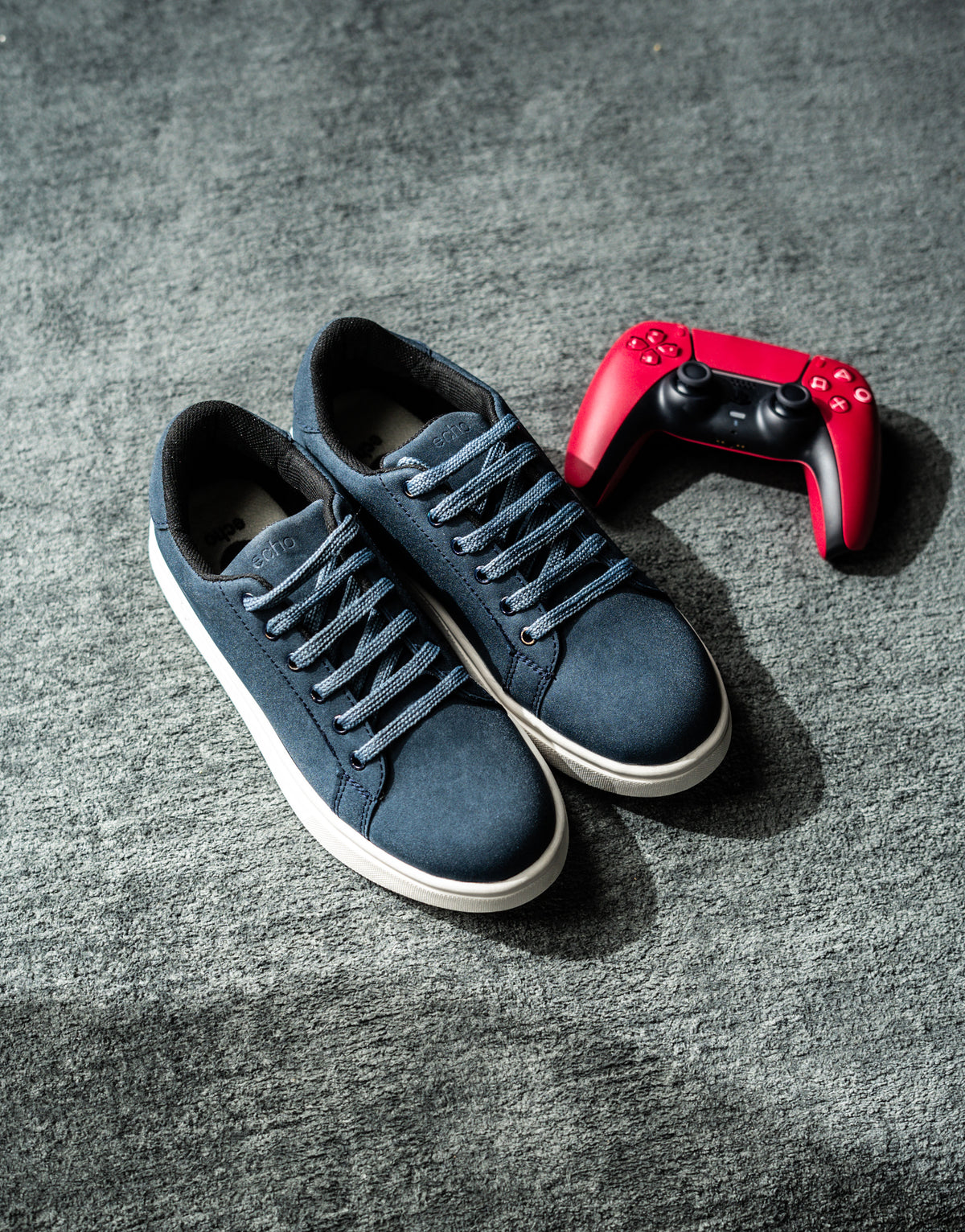 Blue sneakers with white soles on a gray surface, next to a red gaming controller.