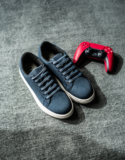Blue sneakers with white soles on a gray surface, next to a red gaming controller.