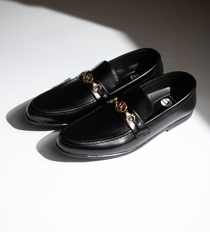 Black loafers with gold accents on a light background