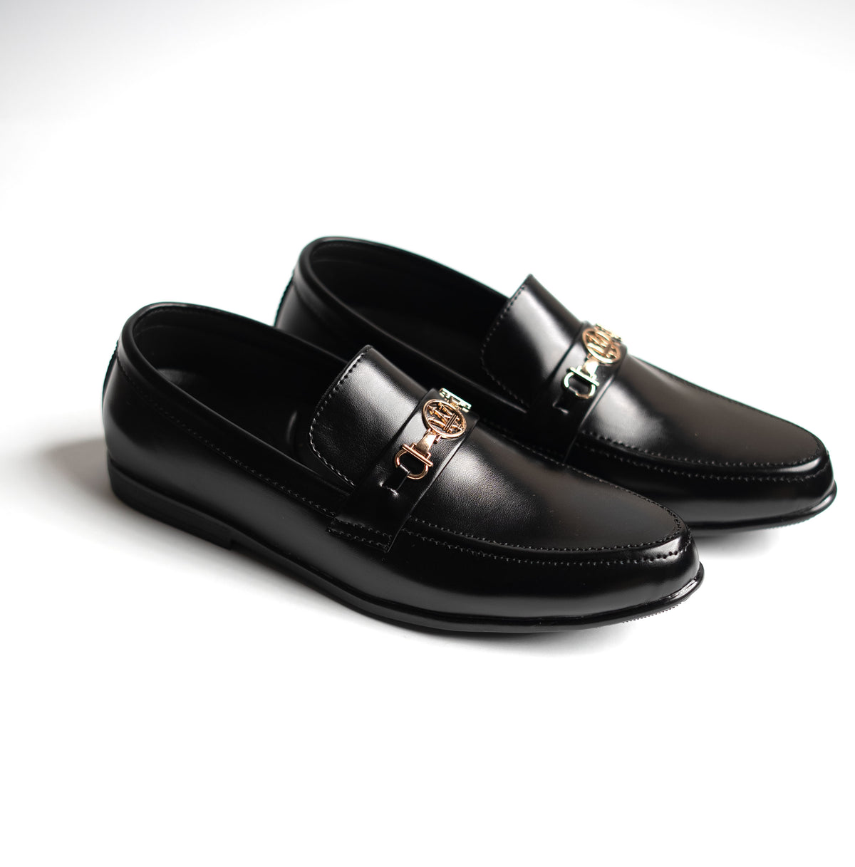Pair of black leather loafers with gold buckles on a white background