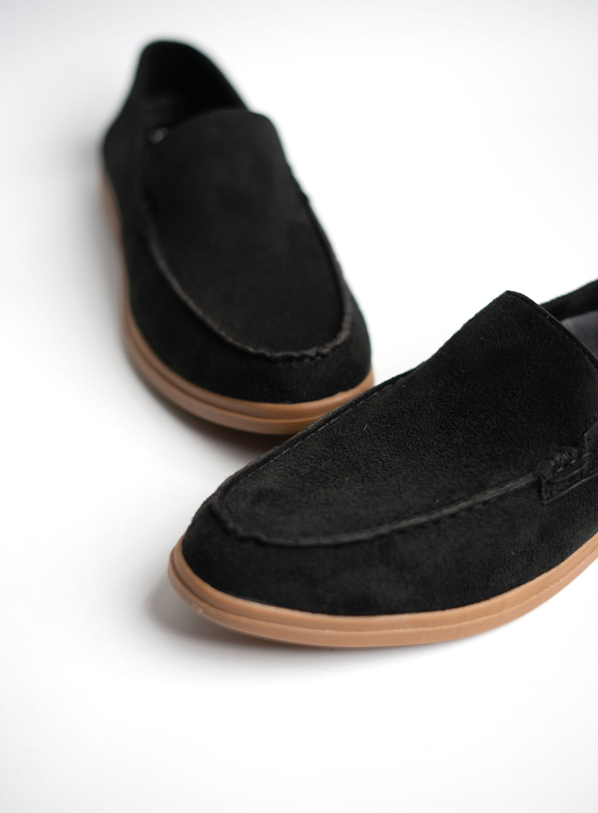 Black slip-on shoes with brown soles on a white background