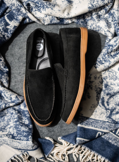 Black loafers with brown soles on a patterned fabric background