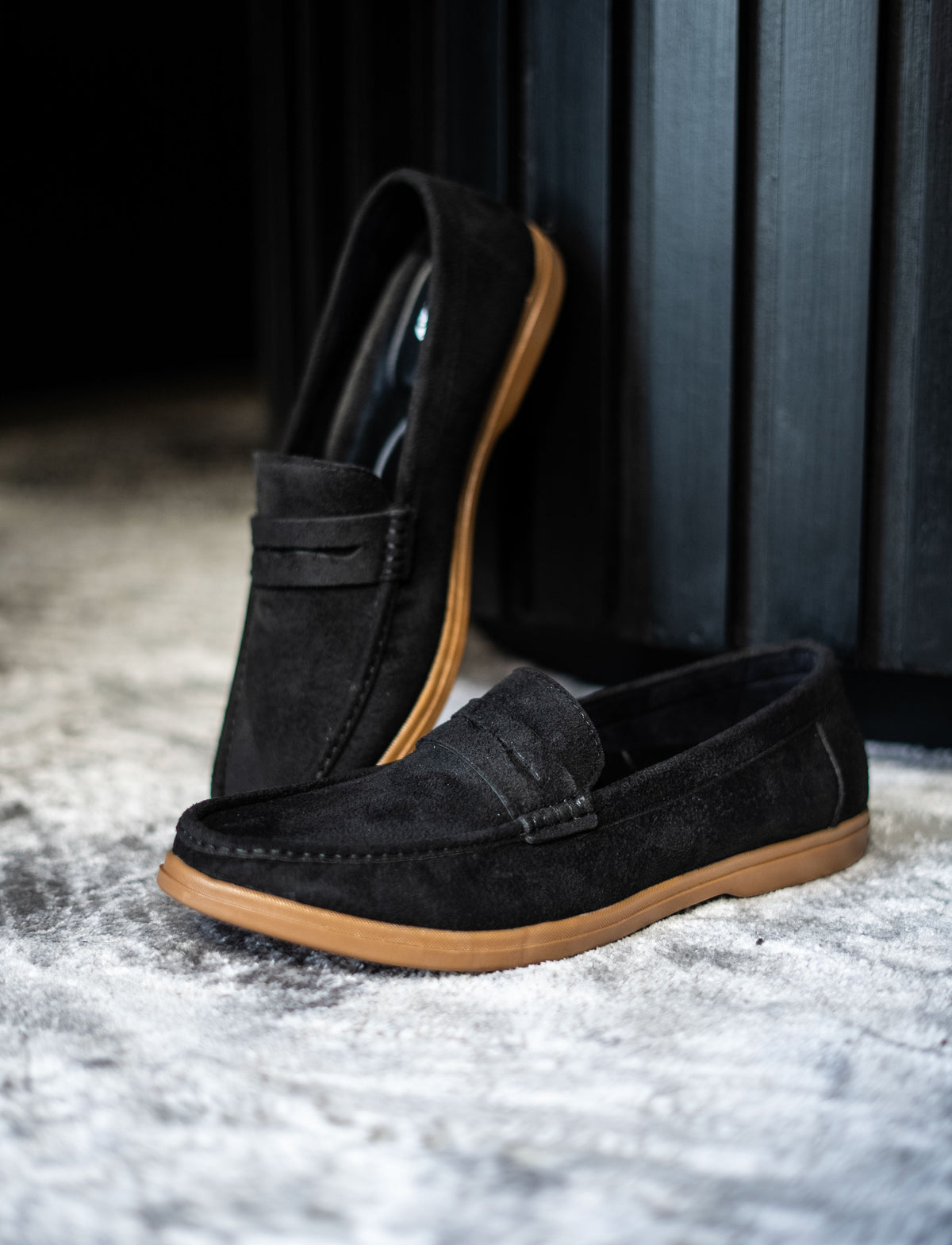 Black loafers with brown soles on a textured surface