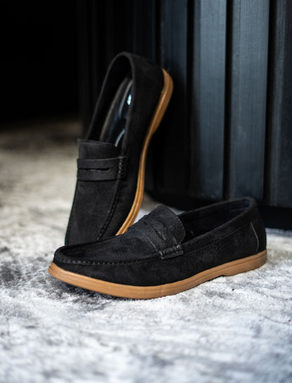 Black loafers with brown soles on a textured surface