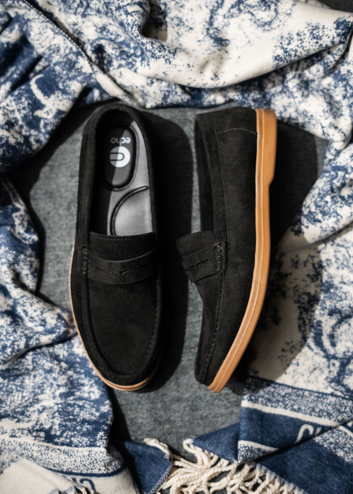 Black loafers with HONEY soles on a textured blue and white fabric background