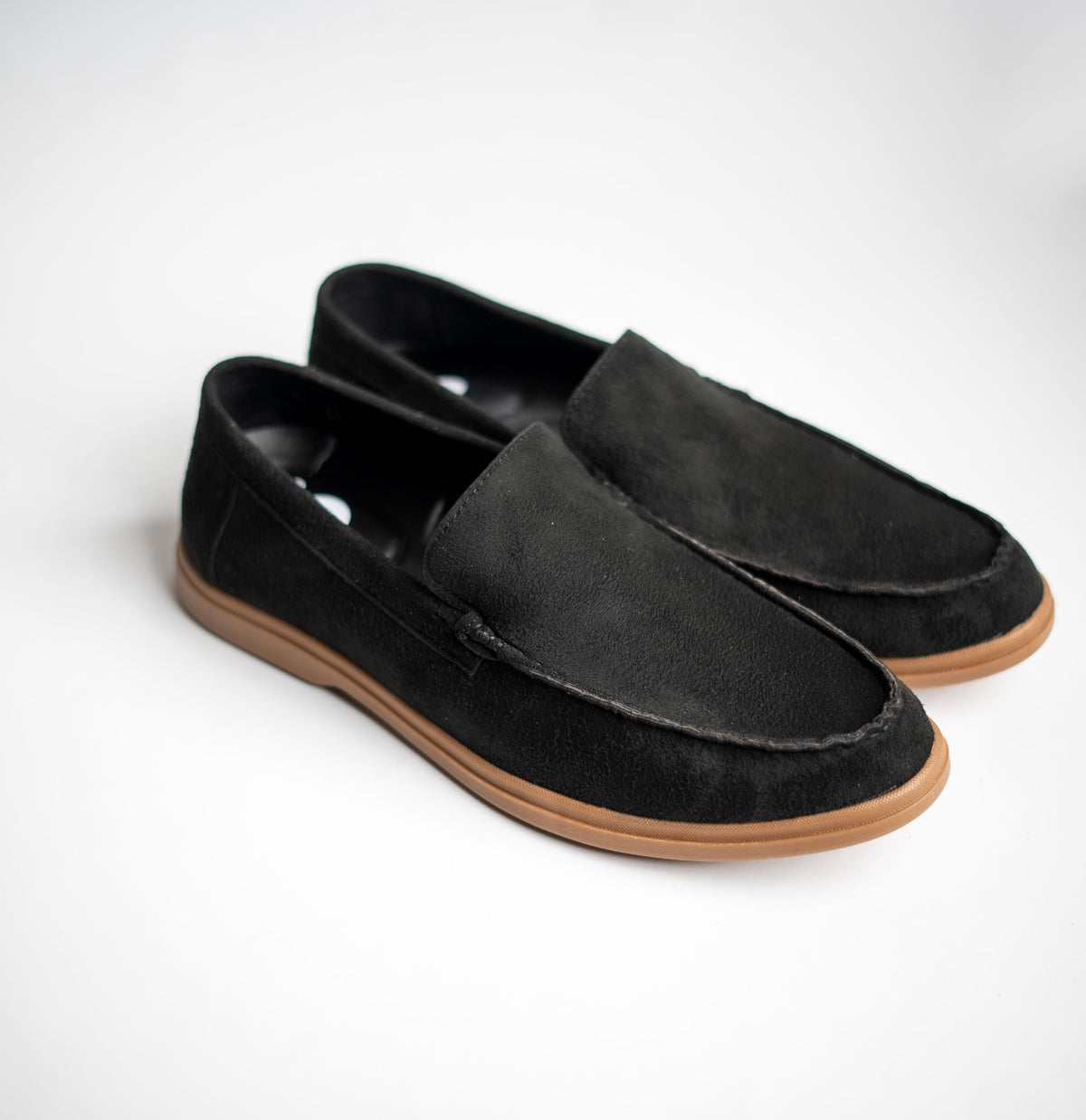 Pair of black loafers with brown soles on a white background