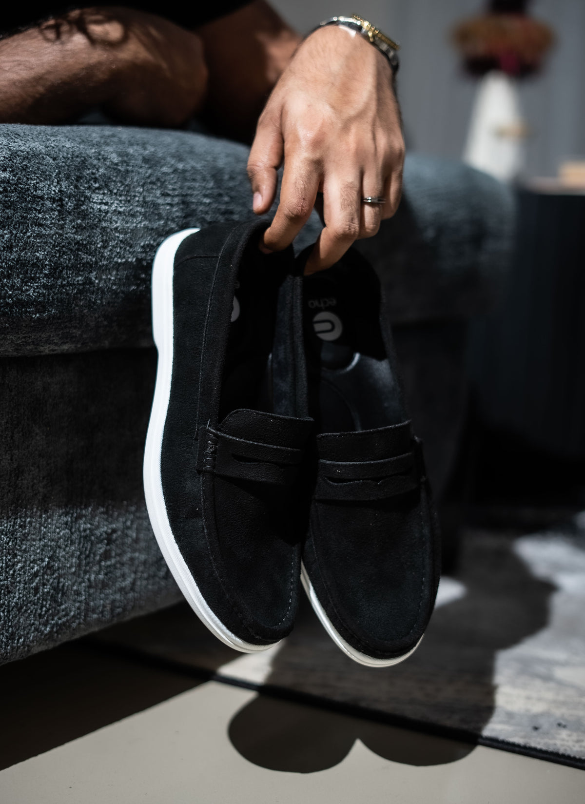 Person holding black slip-on shoes with white soles on a textured surface
