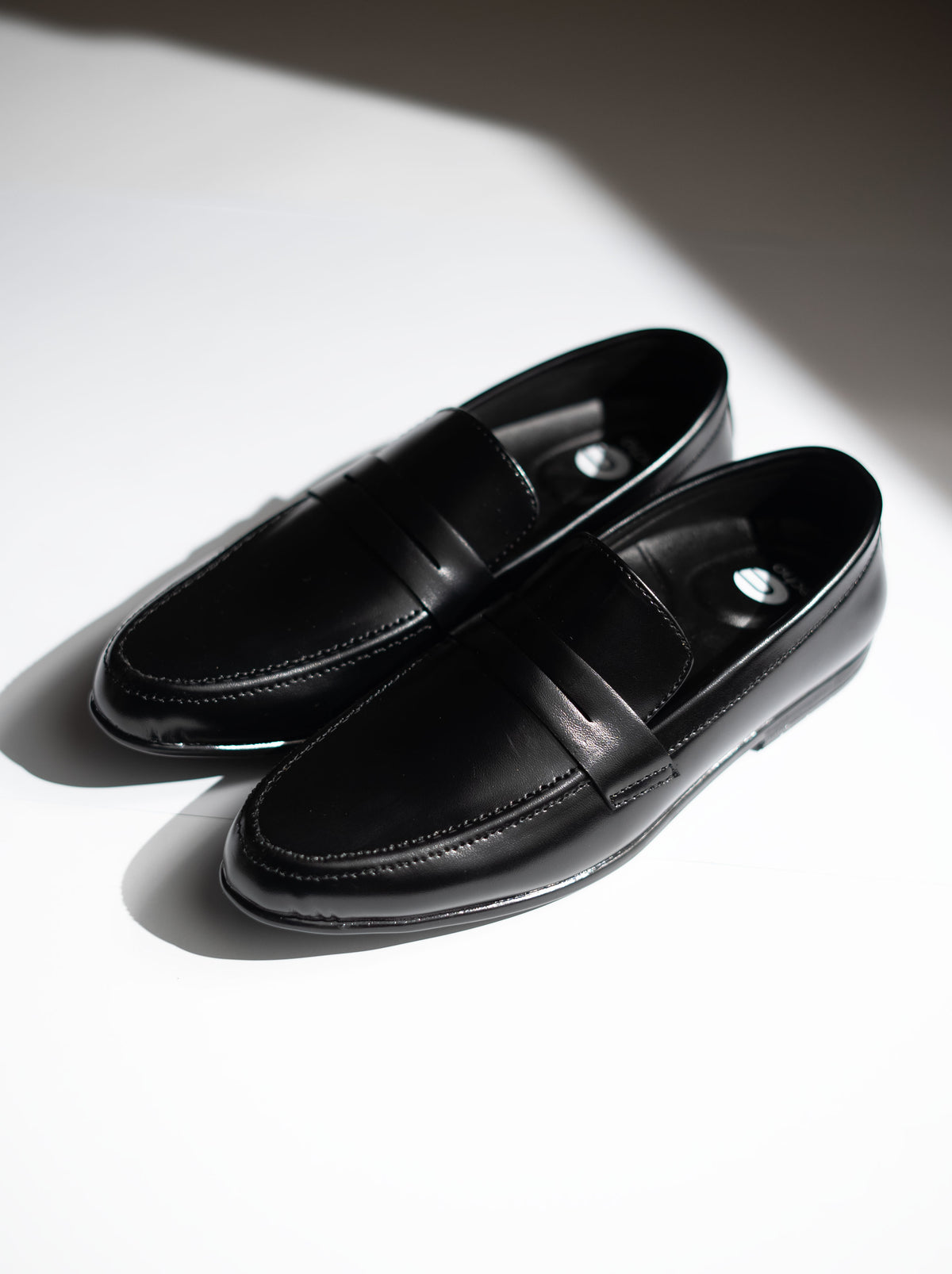 Pair of black loafers on a white surface with a soft shadow.