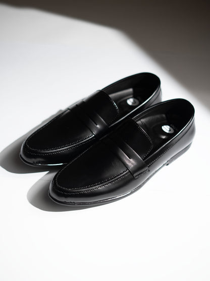 Pair of black loafers on a white surface with a soft shadow.
