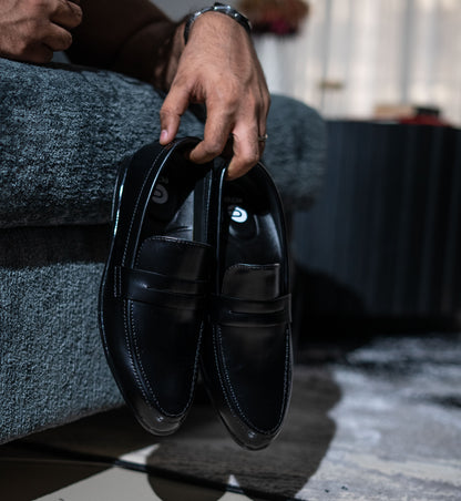 Person holding a pair of black leather shoes with a blurred background