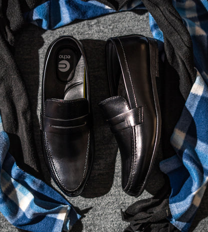Pair of black loafers on a textured surface with a blue and gray patterned fabric.