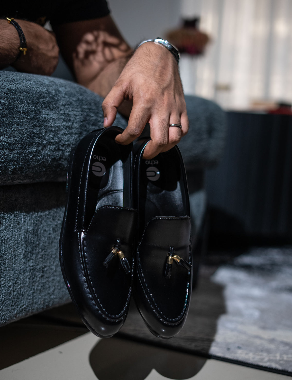Person holding a pair of black loafers with a blurred indoor background