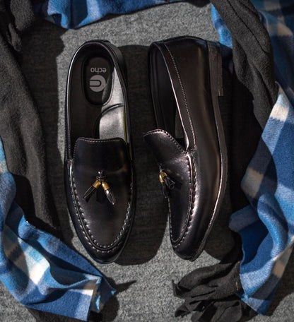 Pair of black loafers on a textured surface with a blue and gray plaid fabric.