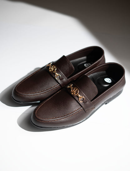 Pair of brown loafers with gold chain detail on a light background