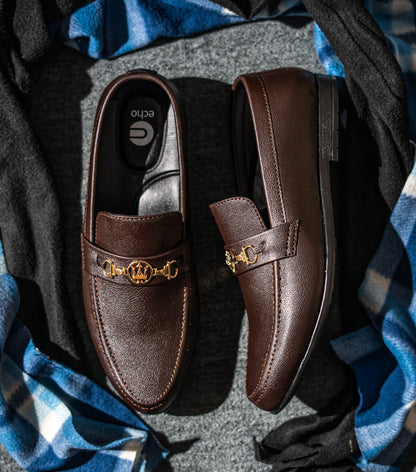 Brown leather loafers with gold accents on a textured surface with blue and gray fabric.