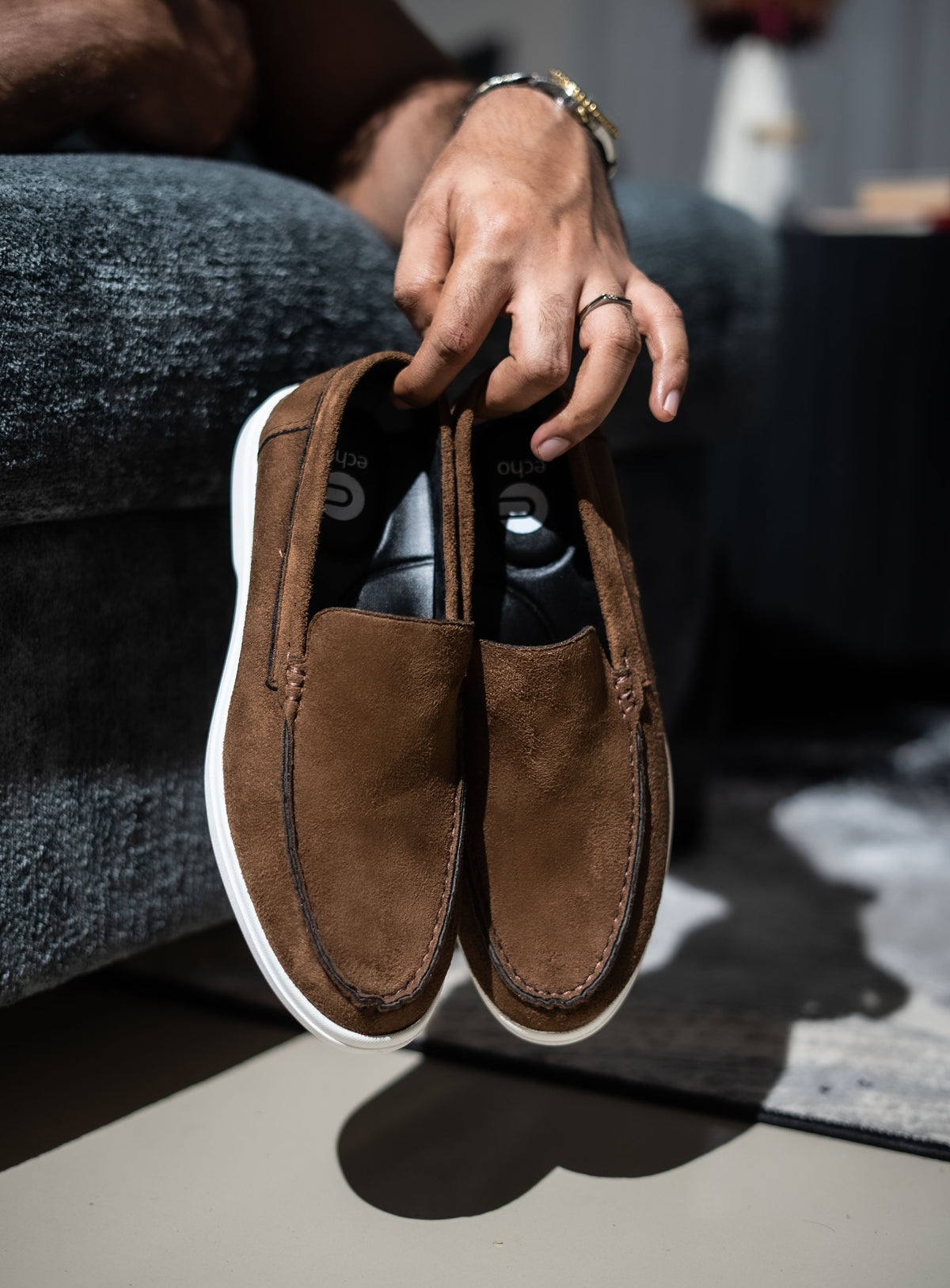 Brown suede loafers being held by a person with a blurred background