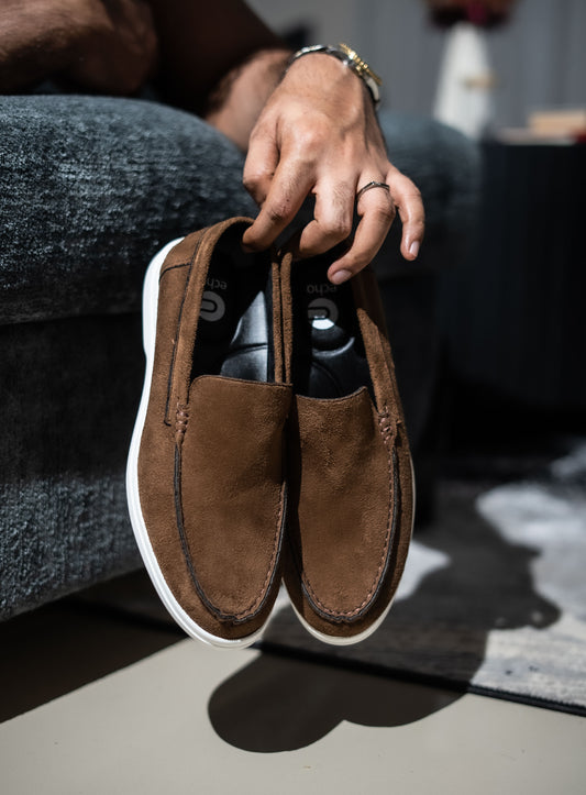 Brown suede loafers being held by a person with a blurred background