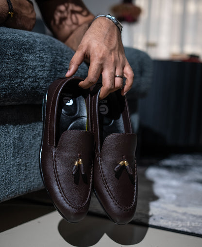 Brown loafers held by a person sitting on a couch.