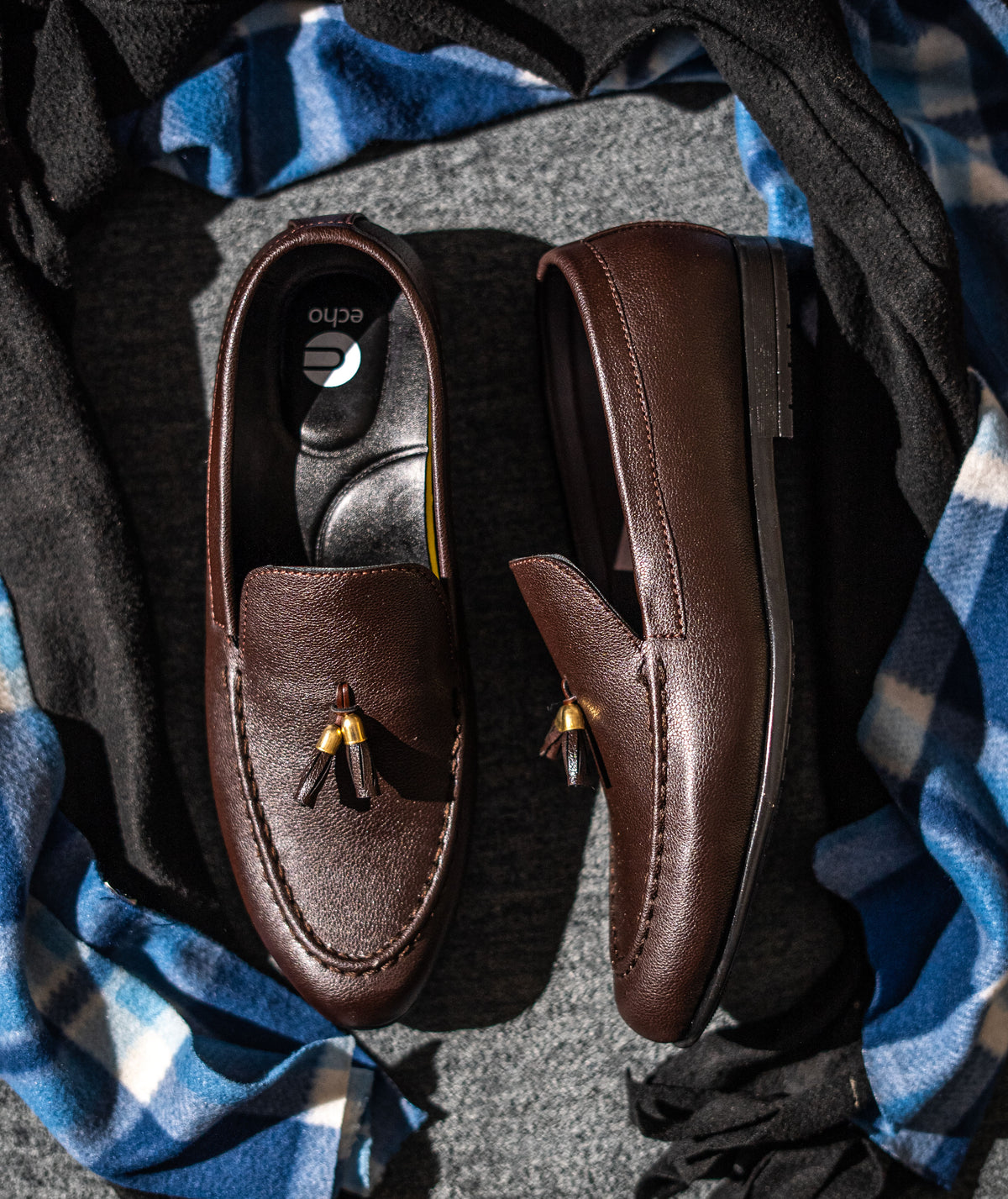 Pair of brown loafers with tassels on a checkered fabric background