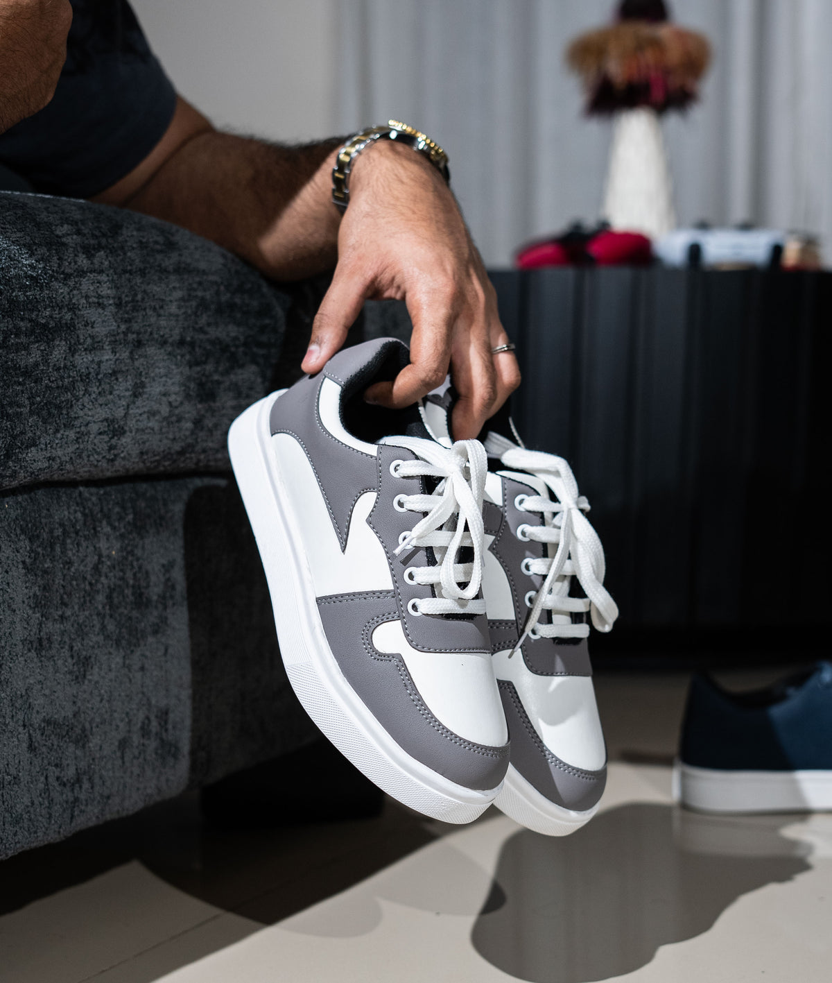 Person holding a pair of gray and white sneakers in an indoor setting.