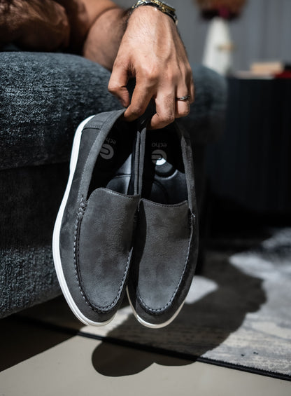Person holding a pair of gray loafers with white soles on a blurred background