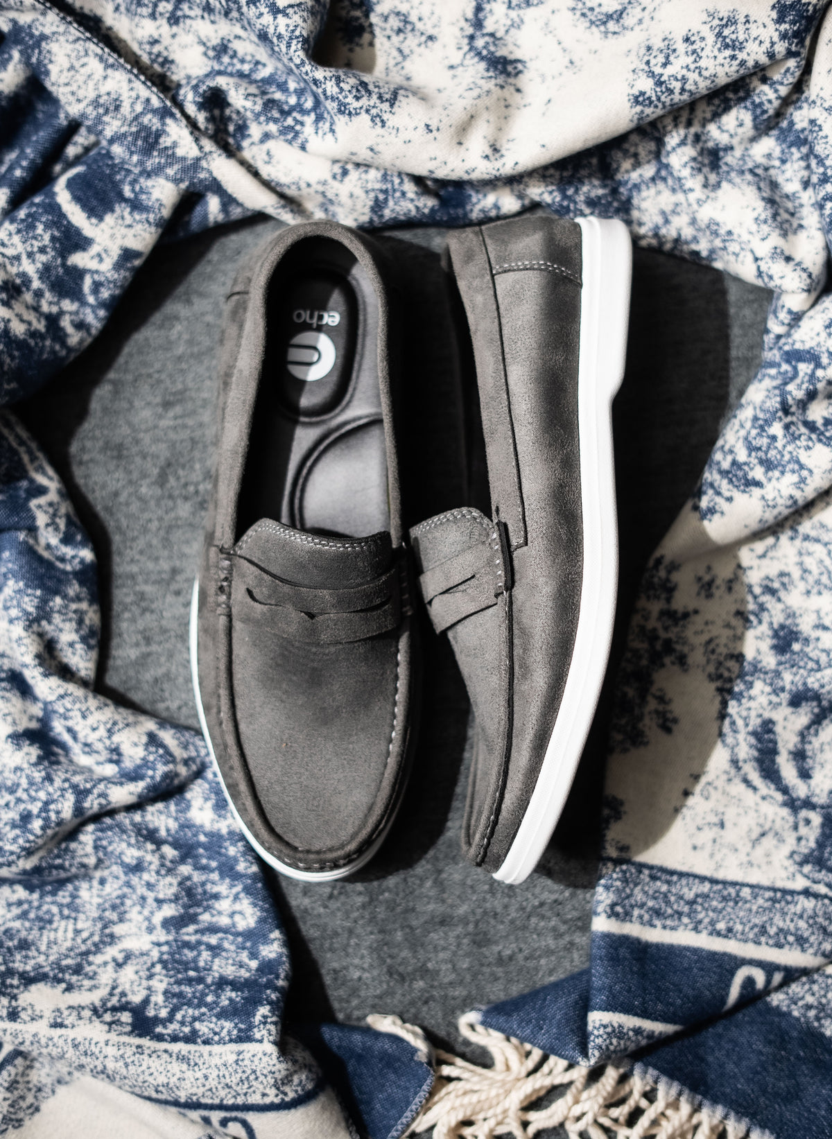 Pair of gray loafers on a textured blue and white fabric background