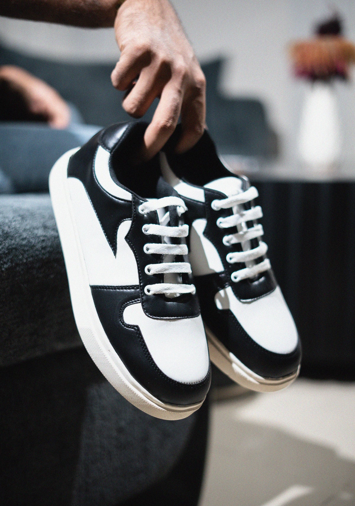 Black and white sneakers being held by a person with a blurred background