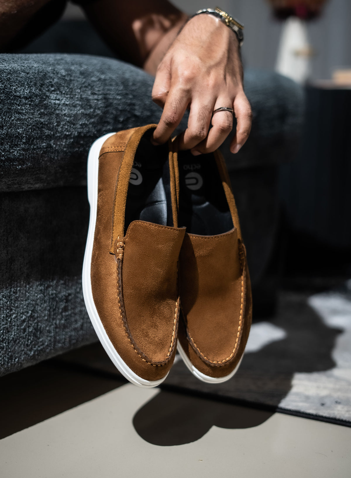 Brown suede loafer shoe held by a person wearing gray jeans.