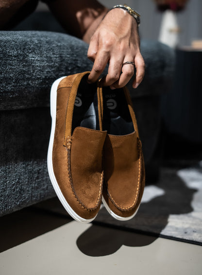 Brown suede loafer shoe held by a person wearing gray jeans.