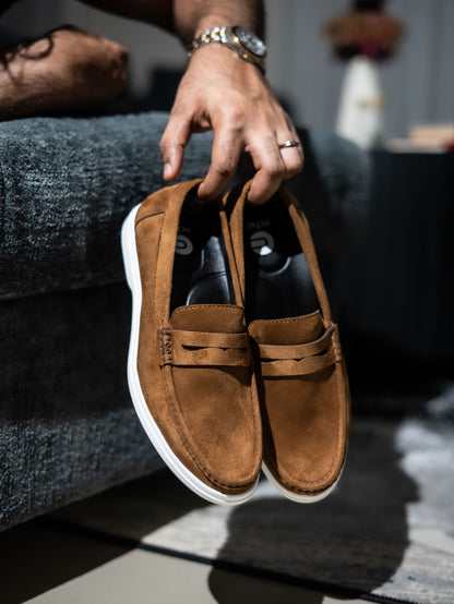 Brown suede loafer shoe held by a person with a blurred background