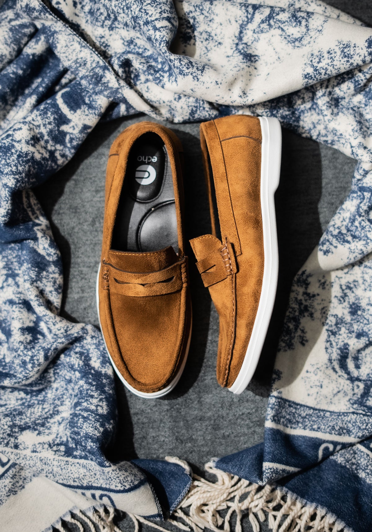 Pair of brown loafers on a textured blue and white fabric background