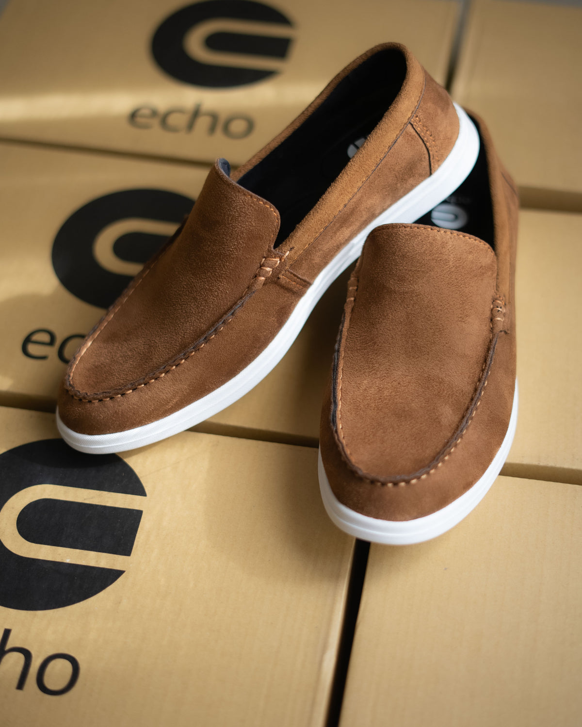 Brown suede loafers on a cardboard surface with 'echo' branding.