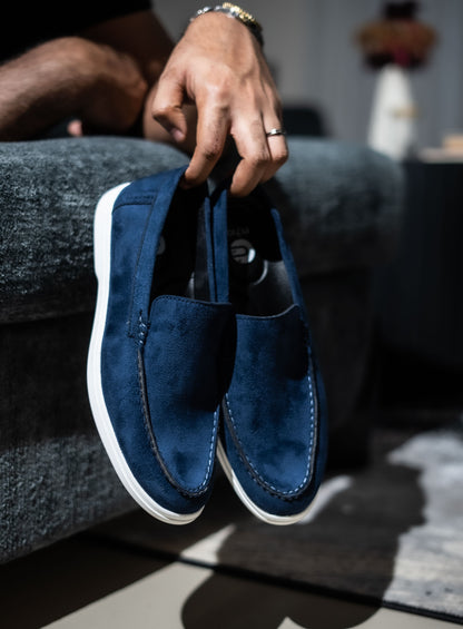 Person holding a pair of blue loafers with a blurred background