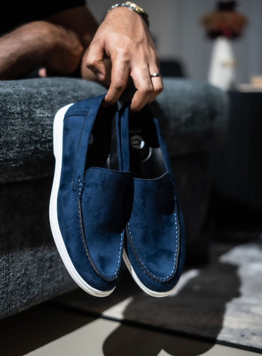 Person holding a pair of blue loafers with a blurred background