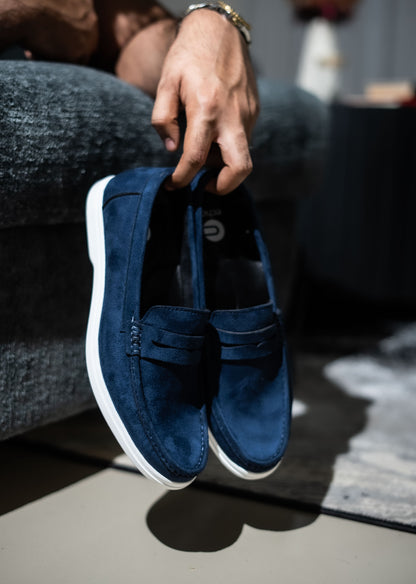 Person holding a pair of blue loafers with white soles.