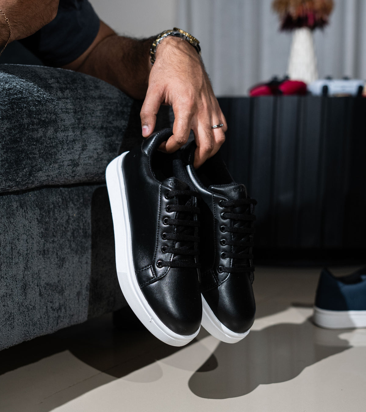 Person holding a pair of black sneakers with white soles on a neutral background