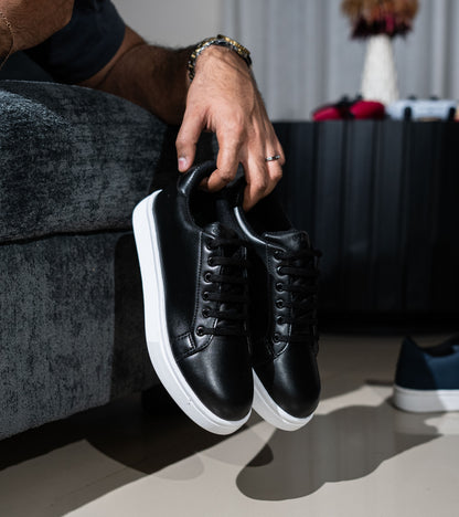 Person holding a pair of black sneakers with white soles on a neutral background
