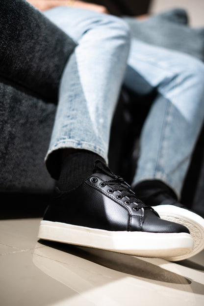 Person wearing black sneakers with white soles and light blue jeans sitting on a gray couch.