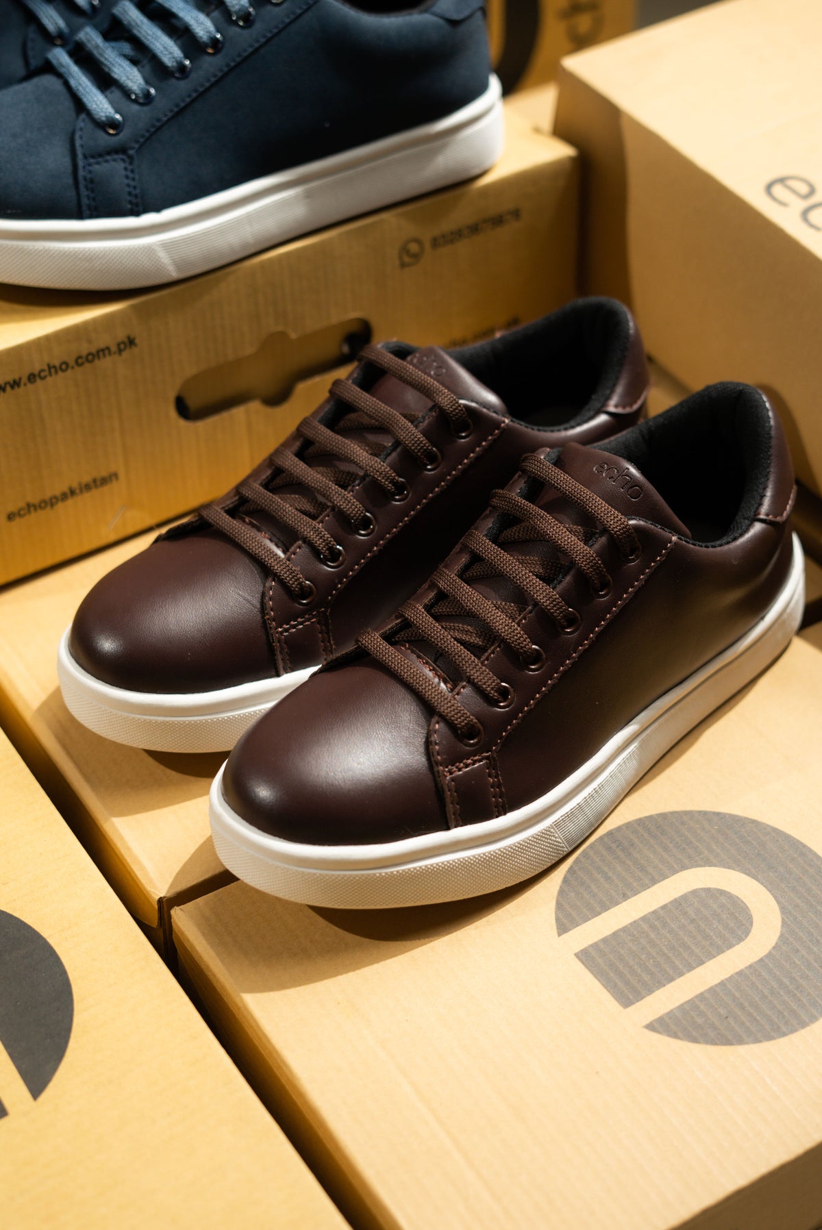 Brown sneakers on a cardboard box with a navy shoe in the background