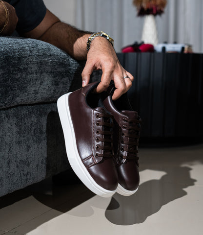 Person holding a pair of brown leather sneakers with white soles.